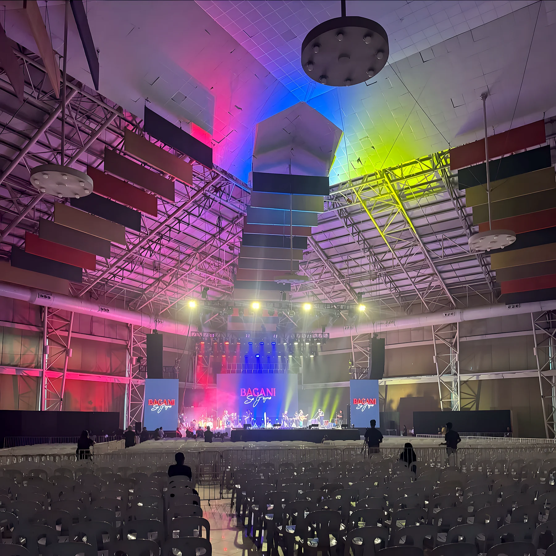 A concert hall with stage lights in pink, blue and yellow and rows of empty chairs.